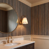 A transitional bathroom featuring a patina brass Gracelyn Wall Sconce with a beige and white linen shade mounted beside a round mirror above marble countertops.