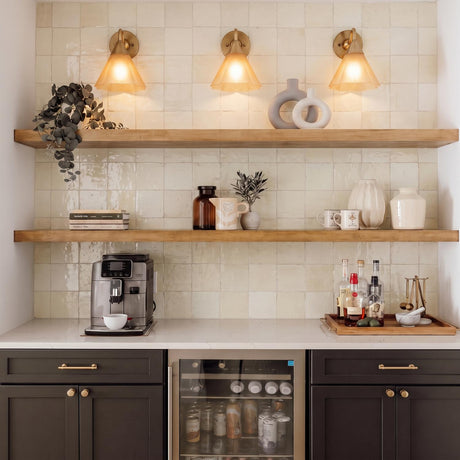 A transitional kitchen bar area with three Catrin wall sconces in aged brass and champagne frosted glass above wood floating shelves and a zellige tile backsplash.