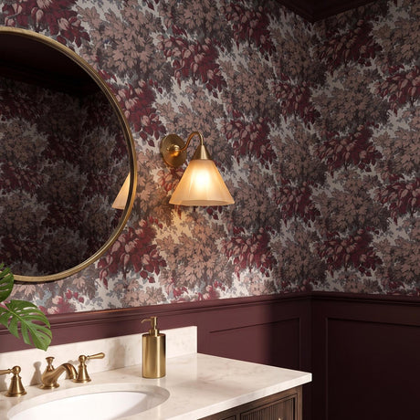 A traditional bathroom featuring a Catrin Wall Sconce in aged brass and champagne frosted glass mounted beside a round mirror against burgundy floral wallpaper and a marble vanity.
