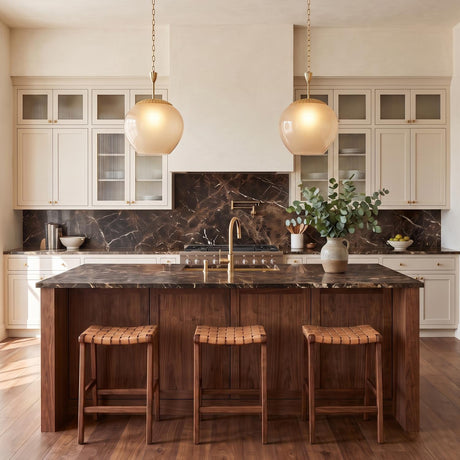 A transitional kitchen with two Annara Medium Pendants in aged brass and champagne frosted glass hanging over a walnut island with dark marble and woven barstools.