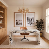 A contemporary office with the Kassia 6 Light Chandelier in aged brass and mirrored champagne glass centered over a white marble waterfall desk and oak built-ins.