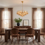 A contemporary dining room features an aged brass chandelier with mirrored champagne glass globes suspended over a dark wood table surrounded by oval-back chairs.