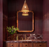 A contemporary bathroom with the Bramble Small Pendant 10 inch in walnut wicker and aged brass hanging over a burgundy marble vanity and fluted plum walls.