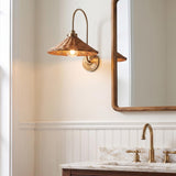A coastal bathroom featuring the Bramble Wall Sconce in walnut wicker and aged brass mounted beside a wood-framed mirror above a marble vanity with beadboard.