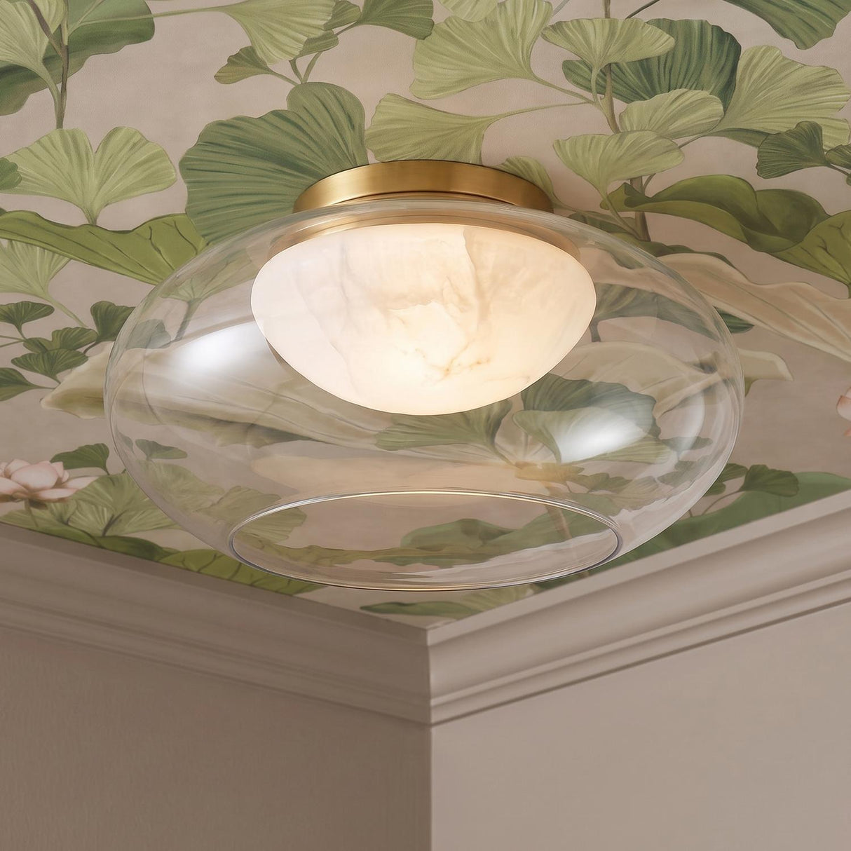 A transitional foyer with the Nadia Medium LED semi-flush mount in aged brass and alabaster installed along a ceiling featuring green ginkgo leaf botanical wallpaper.