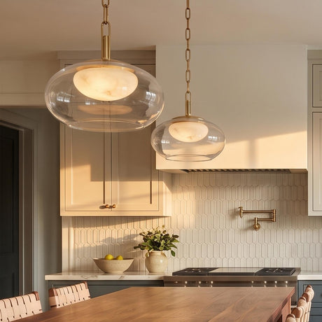 A transitional kitchen with two Nadia Small LED Pendants in aged brass and alabaster suspended over a walnut island beside a white picket tile backsplash.