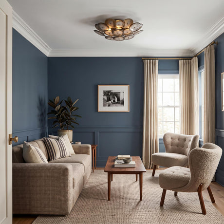 A transitional living room featuring the Perenna Semi-Flush in patina brass and smoke taupe glass above blue paneled walls, beige boucle armchairs, and a walnut coffee table.