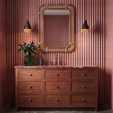 A contemporary bathroom featuring two matte black cone pendants with woven rope trim flanking a cane mirror above a walnut vanity and pink fluted tiles.