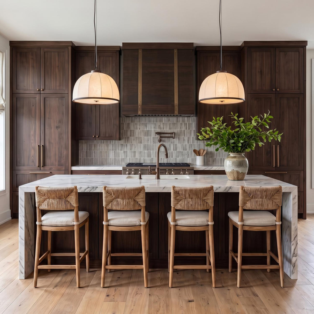 A transitional kitchen with two Emiko Large Pendants featuring a bronze leaf finish and paper shade over a white marble waterfall island with dark walnut cabinets.