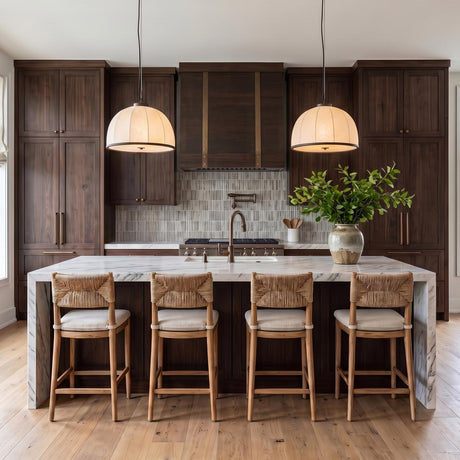 A transitional kitchen with two Emiko Large Pendants featuring a bronze leaf finish and paper shade over a white marble waterfall island with dark walnut cabinets.