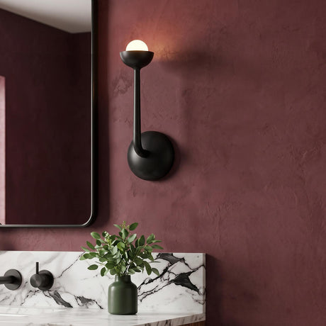 A contemporary bathroom with the Bettina LED Wall Sconce 12", Urban Bronze featuring a matte finish and frosted glass bulb mounted on burgundy walls beside a marble vanity.
