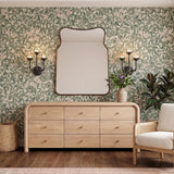 A transitional bedroom with the Bettina LED 3 Light Wall Sconce in urban bronze flanking a curved mirror above a light wood dresser and floral wallpaper.