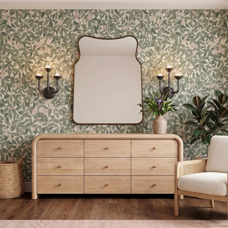 A transitional bedroom with the Bettina LED 3 Light Wall Sconce in urban bronze flanking a curved mirror above a light wood dresser and floral wallpaper.