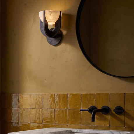 A modern bathroom with an Armand LED Wall Sconce 8", Urban Bronze and Alabaster mounted beside a round black mirror over ochre zellige tile and marble vanity.