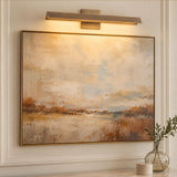 A transitional living room featuring the Avel LED Picture Light 23" in vintage brass mounted above framed abstract wall art and decorative wall molding.