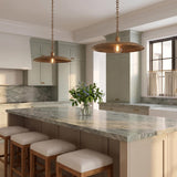 A transitional kitchen with two Crawford Large Pendant 19", Patina Brass pendants hanging over a gray marble island with sage green cabinetry and upholstered wooden stools.