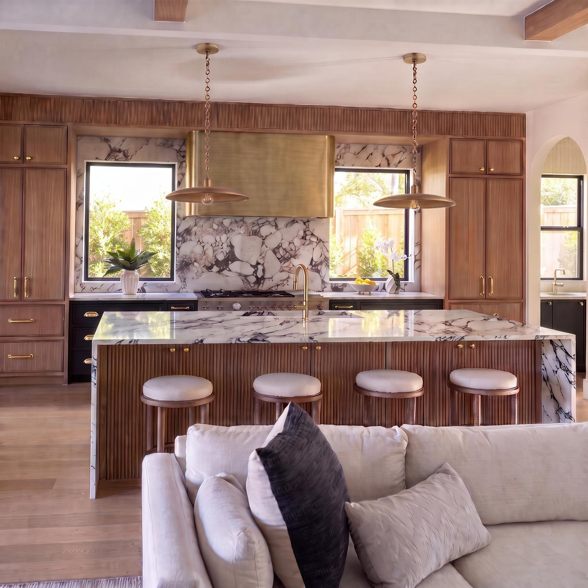 A contemporary kitchen with two Crawford Large Pendants in patina brass hanging over a fluted wood island with a marble waterfall countertop and natural wood ceiling beams.