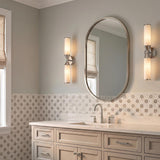 A transitional bathroom with two polished nickel and cloud glass wall sconces flanking an oval mirror above a white quartz vanity and floral patterned tile.