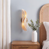 A coastal bedroom with the Xyra Wall Sconce in aged brass and raffia mounted on a light blue wall beside an arched cane headboard and wood nightstand.