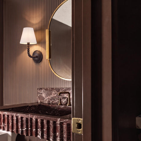 A moody contemporary bathroom featuring a Casimir Curved Wall Sconce in Aged Iron beside a brass mirror above a fluted red marble vanity.