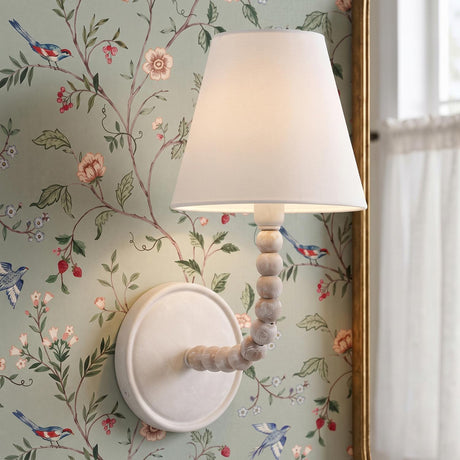 A traditional bedroom featuring the Casimir Curved Wall Sconce 13", Matte Chalk with white wood beads and a linen shade mounted on sage green floral bird wallpaper.