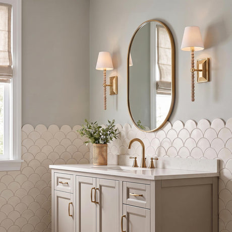 A transitional bathroom with two Casimir Wall Sconce 17", Gilded Brass fixtures with linen shades flanking an oval mirror above a vanity with scalloped tile backsplash.