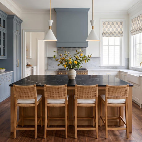 A transitional kitchen featuring two Errol Small LED Pendants in a modern brass and matte white finish suspended over a black marble island with woven barstools.
