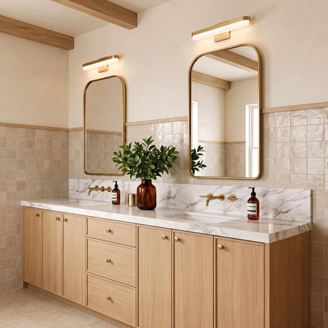 A modern farmhouse bathroom featuring two Harbor LED Vanity Light 18", Modern Brass fixtures in brushed brass above gold mirrors, a white marble countertop, and beamed ceilings.