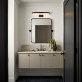 A modern bathroom with the Harbor LED Vanity Light 18", Matte Black mounted over a rounded black mirror and marble countertop with beige floating cabinets.