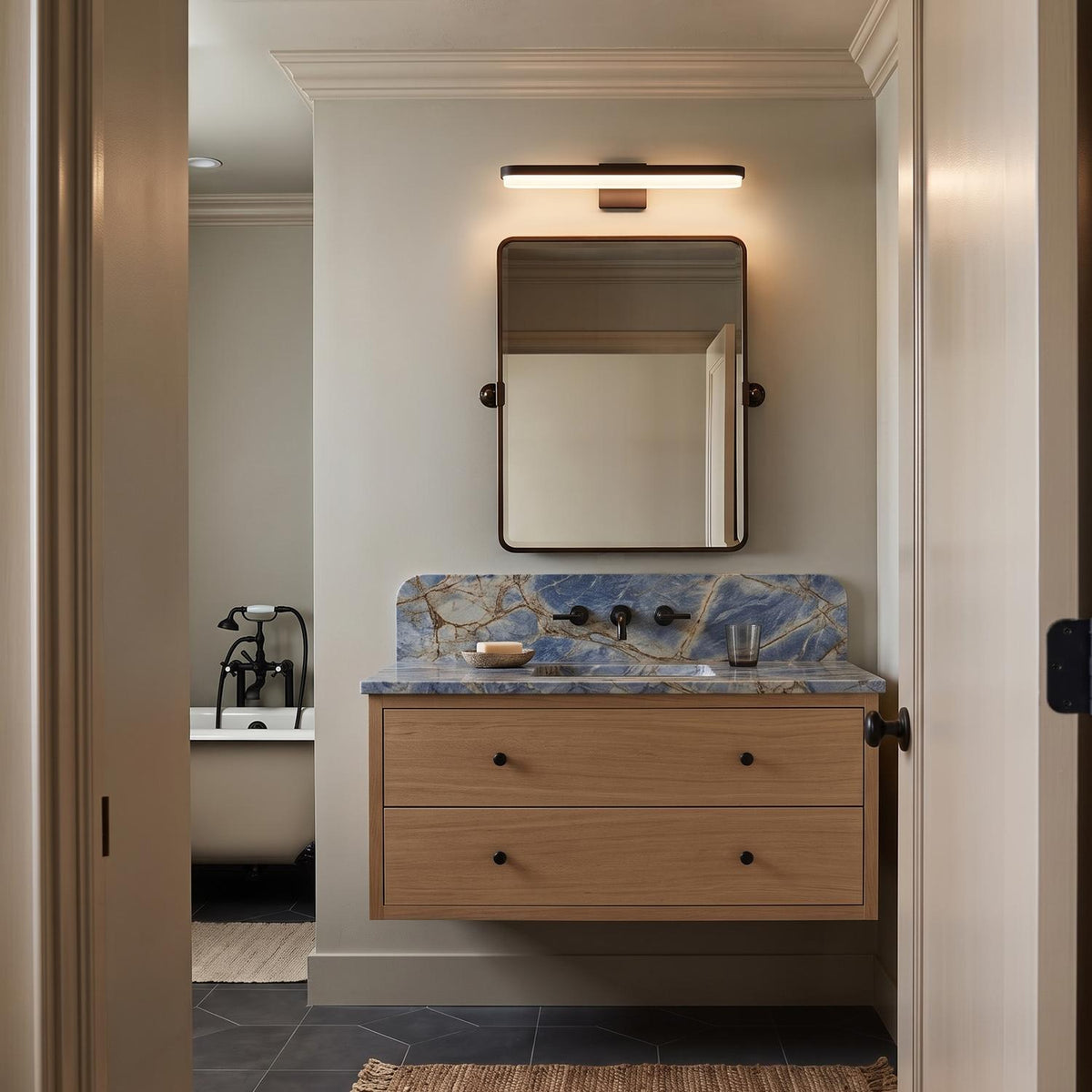 A transitional bathroom with the matte black Harbor LED Vanity Light 27-inch mounted over a blue marble backsplash, floating natural wood vanity, and dark hexagonal flooring.