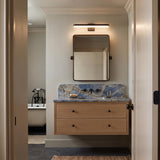 A transitional bathroom with the matte black Harbor LED Vanity Light 27-inch mounted over a blue marble backsplash, floating natural wood vanity, and dark hexagonal flooring.