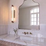 A transitional bathroom with the Halden LED Wall Sconce in weathered brass and ribbed glass mounted beside a curved mirror above a white marble countertop.