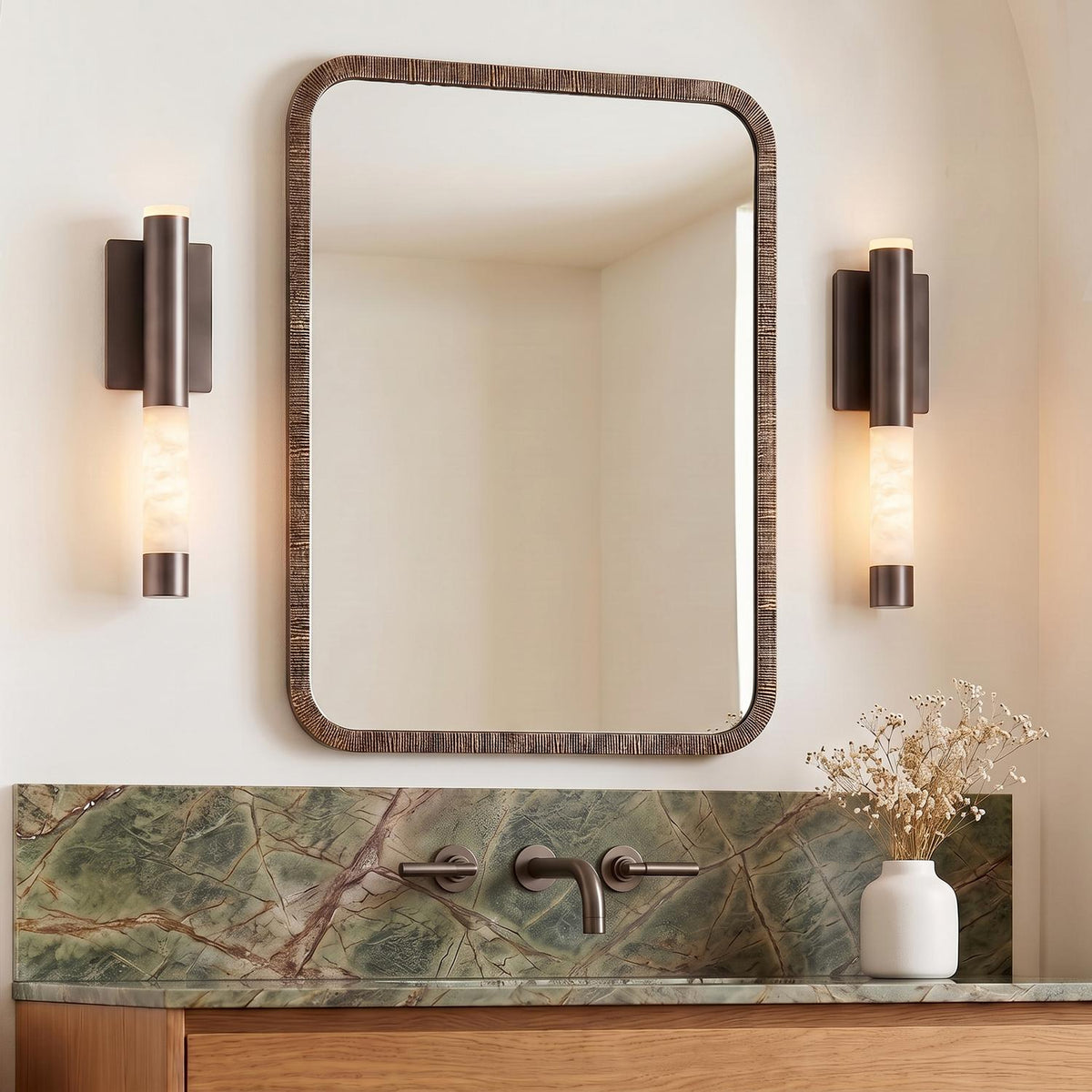 A contemporary bathroom with the Anders Medium LED Wall Sconce in pewter bronze and alabaster flanking a textured mirror above a green marble backsplash and wood vanity.