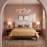 A mid-century bedroom with the Zinnia Chandelier in satin brass and clear hammered glass centered over a walnut bed frame and soft mauve walls.