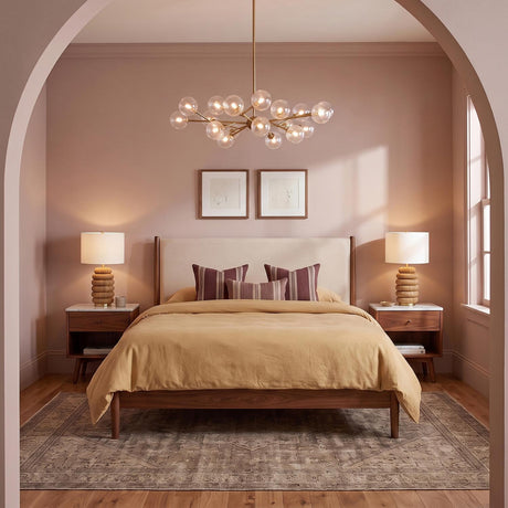 A mid-century bedroom with the Zinnia Chandelier in satin brass and clear hammered glass centered over a walnut bed frame and soft mauve walls.