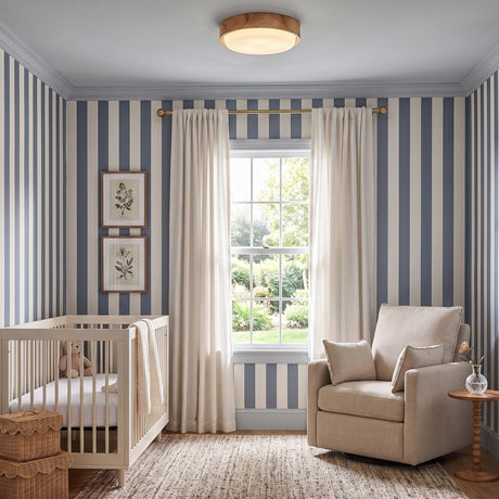 A transitional nursery with a natural wood and opal glass flush mount along the blue ceiling, featuring blue and white striped wallpaper and a white wooden crib.