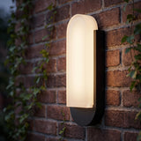 A traditional red brick exterior wall at twilight with the Locke Outdoor LED Wall Sconce in textured black and frosted glass glowing beside climbing green ivy.