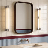 A transitional bathroom featuring two Lavinia LED Wall Sconces in polished nickel and opal glass flanking a wood-framed mirror over a beige stone countertop.