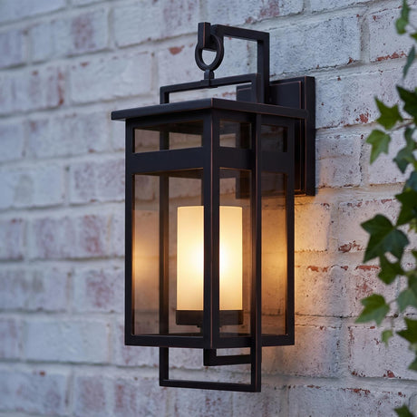 A transitional home exterior with the Lansing Outdoor Wall Light in dark bronze glowing on a whitewashed brick wall at dusk, framed by green ivy vines.