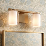 A transitional bathroom featuring the Orlando 2 Light Vanity 14", Satin Brass mounted above a matching brass-framed mirror against muted blue and beige floral wallpaper.