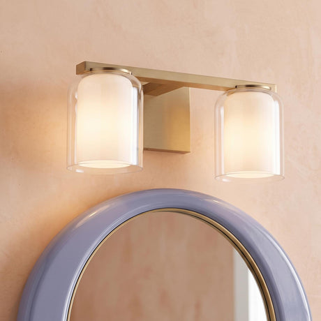 A contemporary bathroom featuring an Orlando 2 Light Vanity 14" in satin brass with glass shades mounted above a glossy periwinkle round mirror against a textured peach wall.