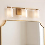 A transitional bathroom featuring the Orlando 3 Light Vanity in satin brass with double-glass shades mounted above a gold-rimmed scalloped wall mirror.