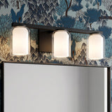 A contemporary bathroom with the Orlando 3 Light Vanity 23", Matte Black featuring clear and frosted glass shades above a black framed mirror against botanical wallpaper.