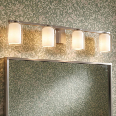 A transitional bathroom features the Orlando 4 Light Vanity 33", Brushed Nickel mounted above a matching framed mirror against green botanical wallpaper.