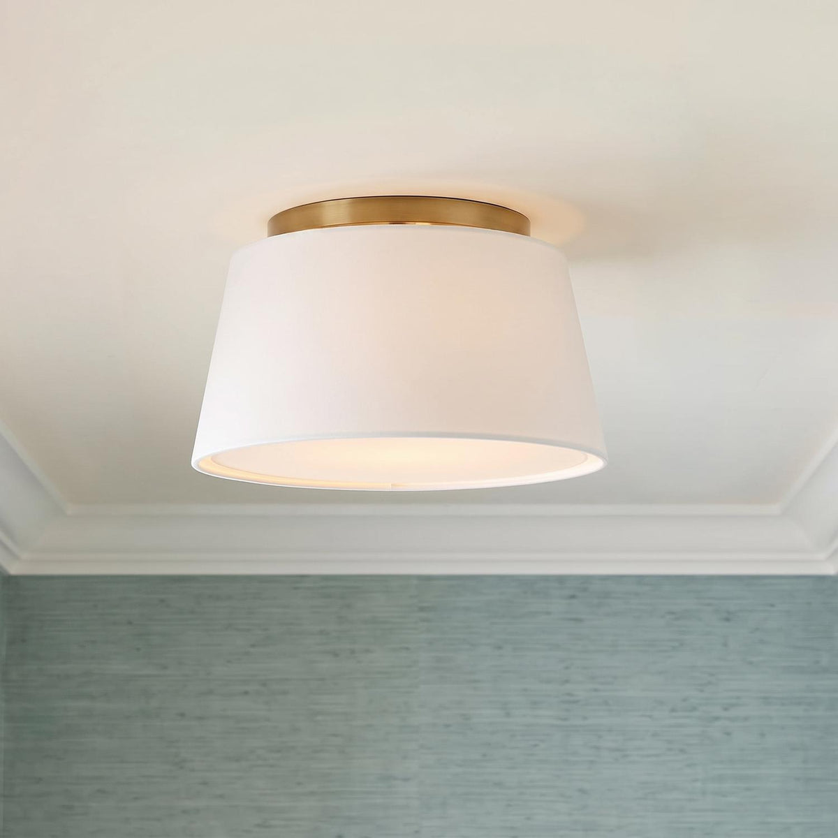 A transitional bedroom featuring the Barton Small Flush Mount 12 inch in aged brass and white linen above blue grasscloth wallpaper and white crown molding.