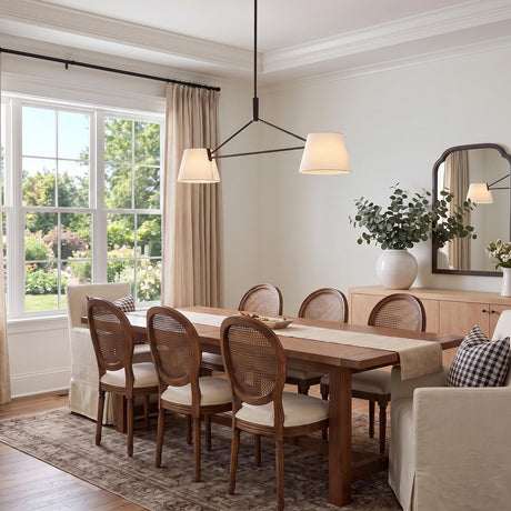 A transitional dining room with the Barton 2 Shade Linear Pendant 56" in aged iron and white linen over a wooden table with cane-back chairs.