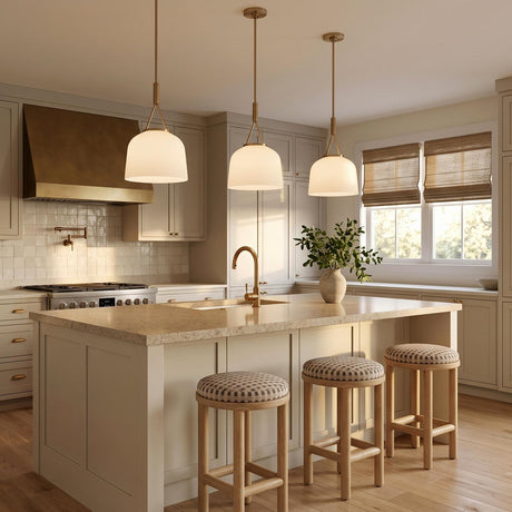 A transitional kitchen with three Stratford Small Pendants in aged brass and opal glass hanging over a beige stone island with neutral cream shaker cabinets.