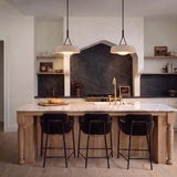 A modern farmhouse kitchen featuring two Stratford Medium Pendants in aged iron and beige over a white marble island with wood cabinets and dark stone backsplash.