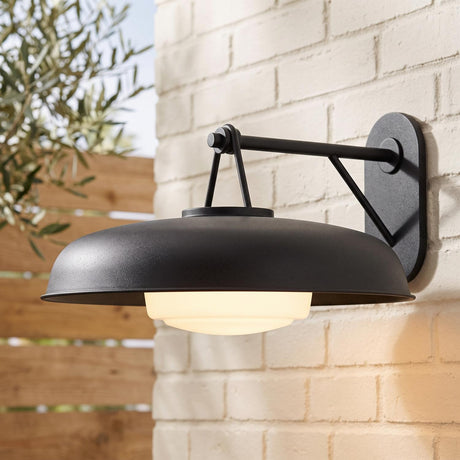A modern farmhouse patio featuring the Stratford Outdoor Wall Sconce, Large, Textured Black mounted on a white brick wall beside an olive tree and wooden fence.