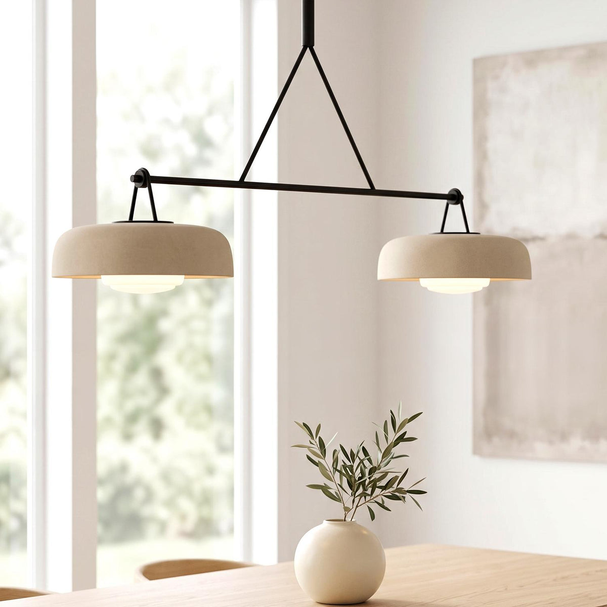 A modern dining room featuring the Stratford 2 Shade Linear Pendant in aged iron and beige over a light wood table with a white ceramic vase.